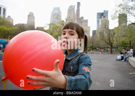 A young girl blowing up a balloon in Central Park, New York City Stock Photo