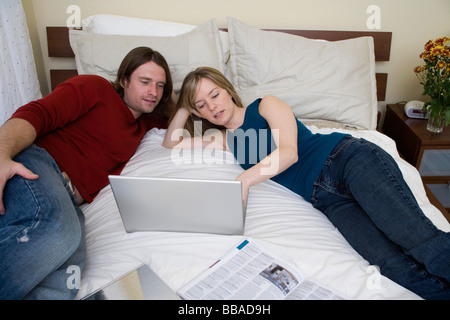A young couple using a laptop on a bed Stock Photo