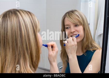 A young woman brushing her teeth in front of a bathroom mirror Stock Photo