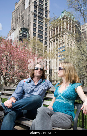 A young couple wearing sunglasses and sitting on a park bench together, Central Park, New York City Stock Photo