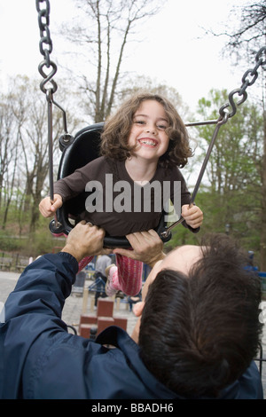 A father pushing his daughter on a swing in a park Stock Photo
