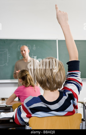 Rear view of a boy raising his hand in a classroom Stock Photo