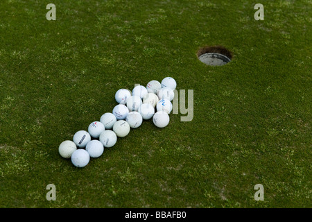 Arrow of golf balls pointing to a hole on a putting green Stock Photo