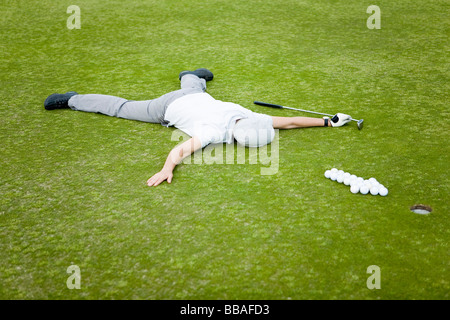 A golfer lying on a putting green behind an arrow of golf balls Stock Photo