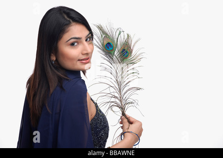 Woman looking at camera, holding peacock feather Stock Photo