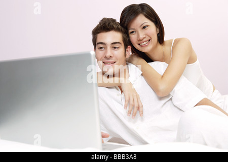 Mixed race couple on bed, looking at laptop, woman hugging man Stock Photo