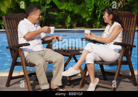 Couple relaxing in deck chairs by the pool, having tea Stock Photo