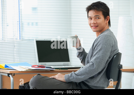 Man with cup relaxing at desk and looking at camera Stock Photo