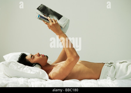 Young man lying in bed, reading and listening to music Stock Photo