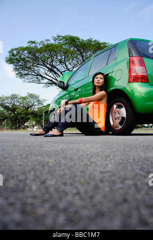 A young woman sits on the ground leaning against a car Stock Photo