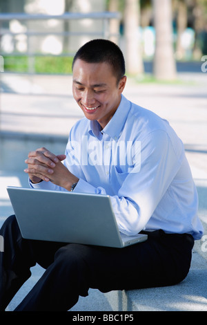 A man smiles as he uses his laptop outdoors Stock Photo