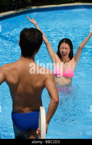 Woman in swimming pool, arms outstretched, looking at man standing in front of her Stock Photo