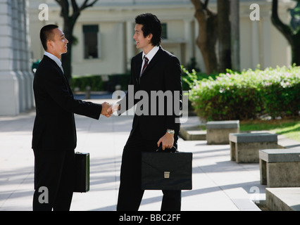 Two men wearing suits greet each other and shake hands in the park Stock Photo