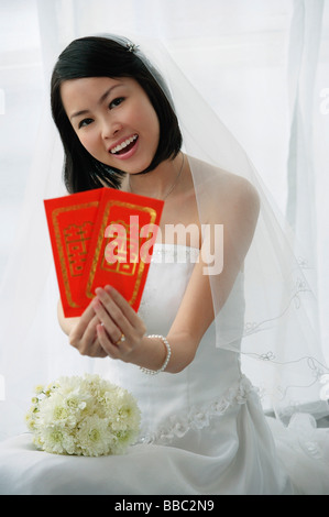 A bride smiles at the camera and holds out two red envelopes Stock Photo