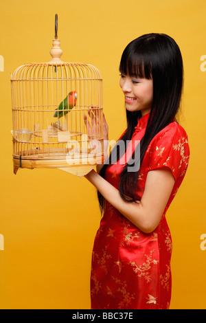 Young woman holding lovebird in bird cage, looking at bird Stock Photo