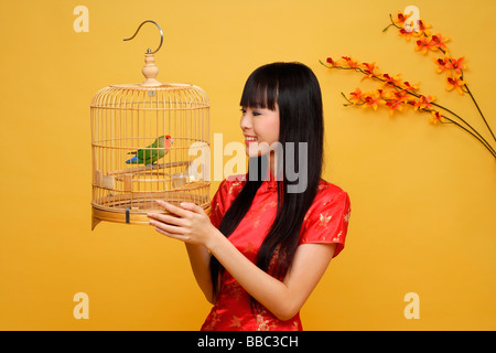 Young woman holding lovebird in bird cage Stock Photo