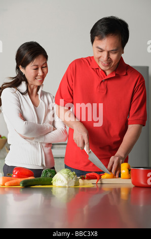 Couple in kitchen, man cutting vegetables, woman watching him Stock Photo