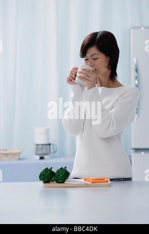Woman in kitchen, drinking from a cup Stock Photo