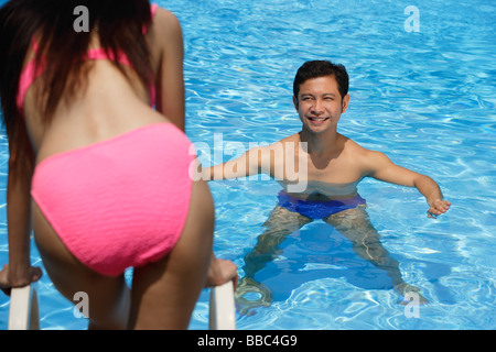Man in swimming pool, smiling at woman standing in front of him Stock Photo