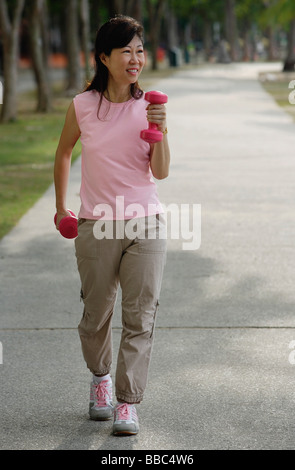 Mature woman using dumbbells, walking along path