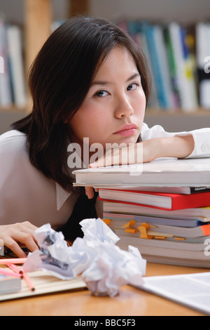 Young woman in library, leaning on books, sad expression Stock Photo