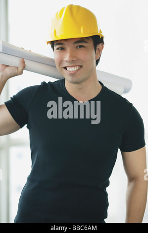 Young adult wearing hardhat, carrying blueprints over his shoulder Stock Photo