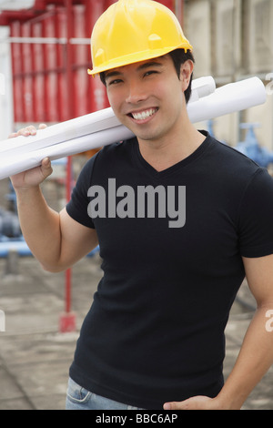 Young man wearing hardhat, carrying blueprints Stock Photo