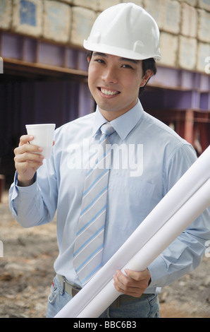 Businessman wearing hardhat, carrying blueprints and a cup Stock Photo