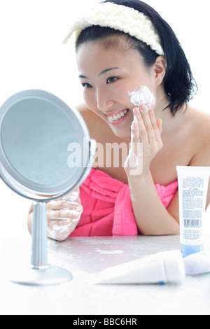 Young woman sitting at dressing table, putting lotion on face Stock Photo