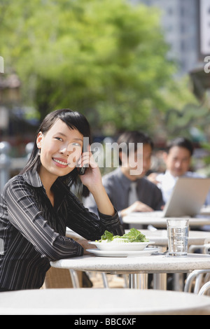 Businesswoman using mobile phone at outdoor cafe, people in the background Stock Photo