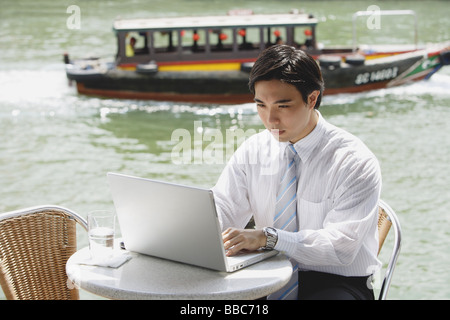Businessman sitting at outdoor cafe, using laptop, river in the background Stock Photo