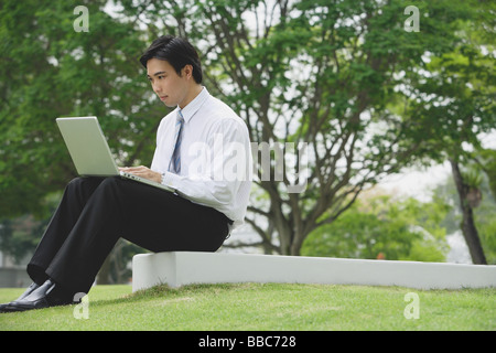 Young businessman sitting in park using laptop Stock Photo