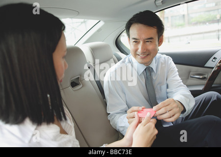 Businessman and businesswoman in backseat of car, exchanging business cards Stock Photo