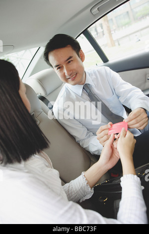 Two businesspeople in backseat of car, exchanging business cards Stock Photo