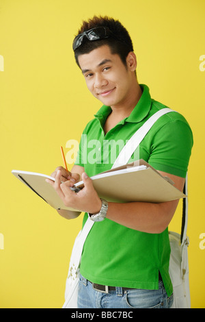 Man standing against yellow background, writing in notebook, looking at camera Stock Photo