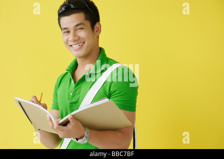 Young man writing in notebook, looking at camera Stock Photo