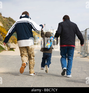 Three generations of one family. A young boy skips between his dad and grandad. Bournemouth seafront. Dorset. UK.