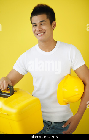 Man carrying construction hat and toolbox, smiling at camera Stock Photo
