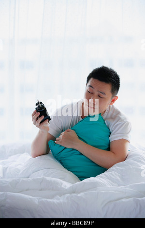 Man sitting in bed, holding alarm clock Stock Photo
