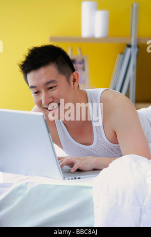 Man lying on bed using laptop Stock Photo