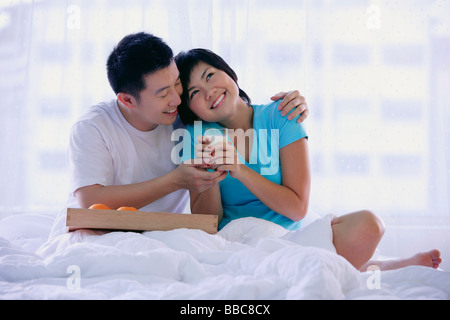 Couple sitting on bed, woman holding glass of milk Stock Photo