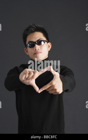 Young man dressed in black, wearing  sunglasses, standing against black background Stock Photo