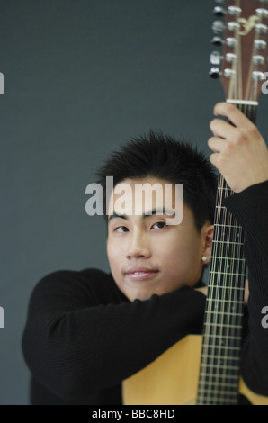 Young man dressed in black leaning on guitar Stock Photo