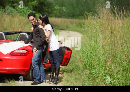 Couple standing next to red sports car, map on the car Stock Photo