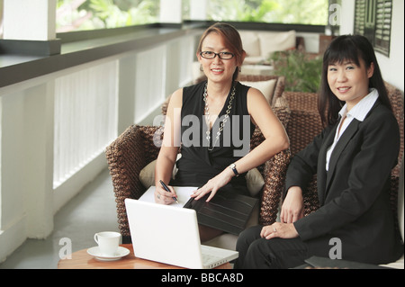 Two businesswomen sitting on patio with laptop, looking at camera Stock Photo