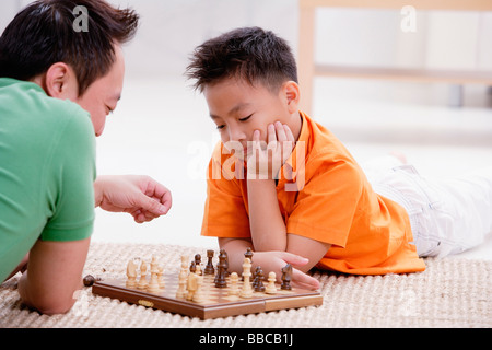 Father and son lying on floor, playing chess Stock Photo