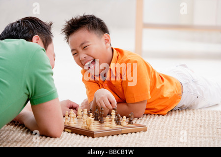 Father and son lying on floor, playing chess, laughing Stock Photo