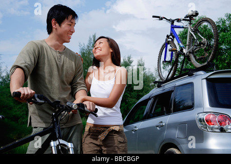 Man on a bike, woman standing next to him, Sports Utility Vehicle in the background Stock Photo