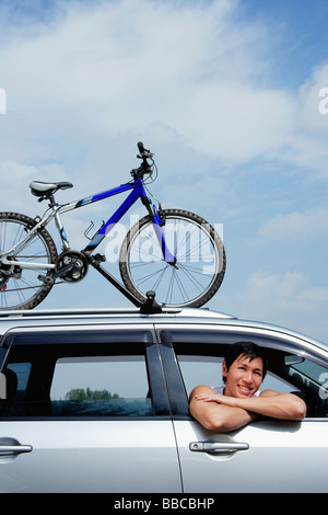 Man leaning out of car window, bicycle on the roof of car Stock Photo