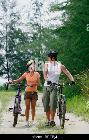 Couple walking with bicycles, looking at each other Stock Photo